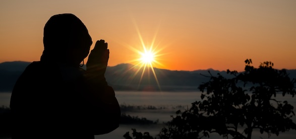 A man prays in front of the setting sun.